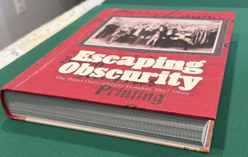 Red clothbound copy of Escaping Obscurity photographed at an angle, showing its front cover and thick page block